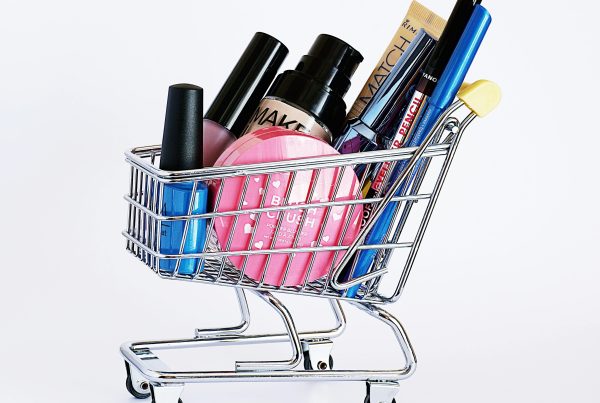 Miniature shopping cart filled with a variety of cosmetics on a white background.